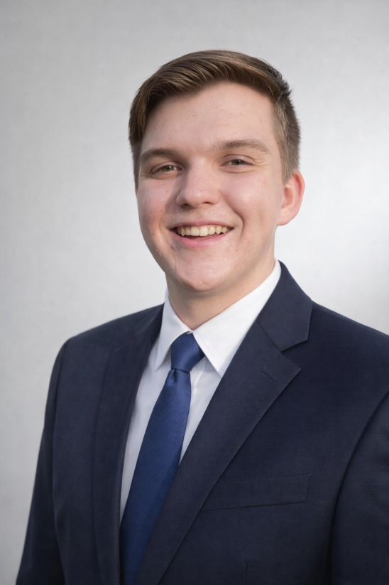 Portrait of Logan Scott in a navy suit and blue tie.